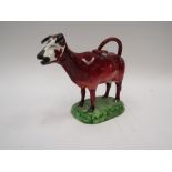 A Staffordshire cow creamer decorated in brown glaze on green base, 13.5cm tall