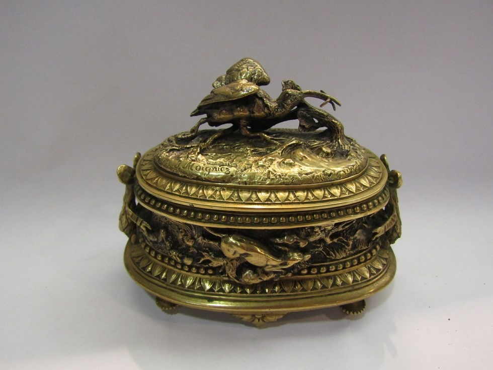 A cast brass lidded pot with hunting scenes of dogs chasing hares, a stork with fish etc. Signed