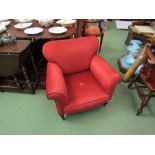 A low armchair upholstered in burnt orange velour, tapering legs and castors