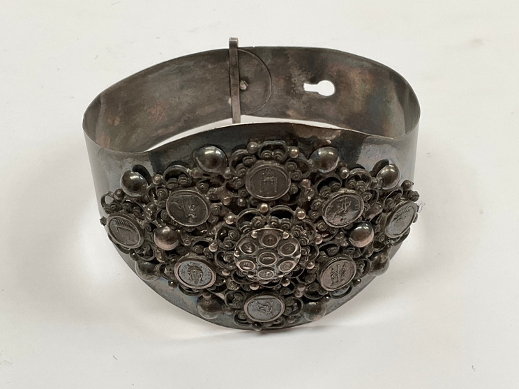 A white metal bangle with pictorial rounders and foliate scrolled decoration