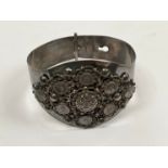 A white metal bangle with pictorial rounders and foliate scrolled decoration