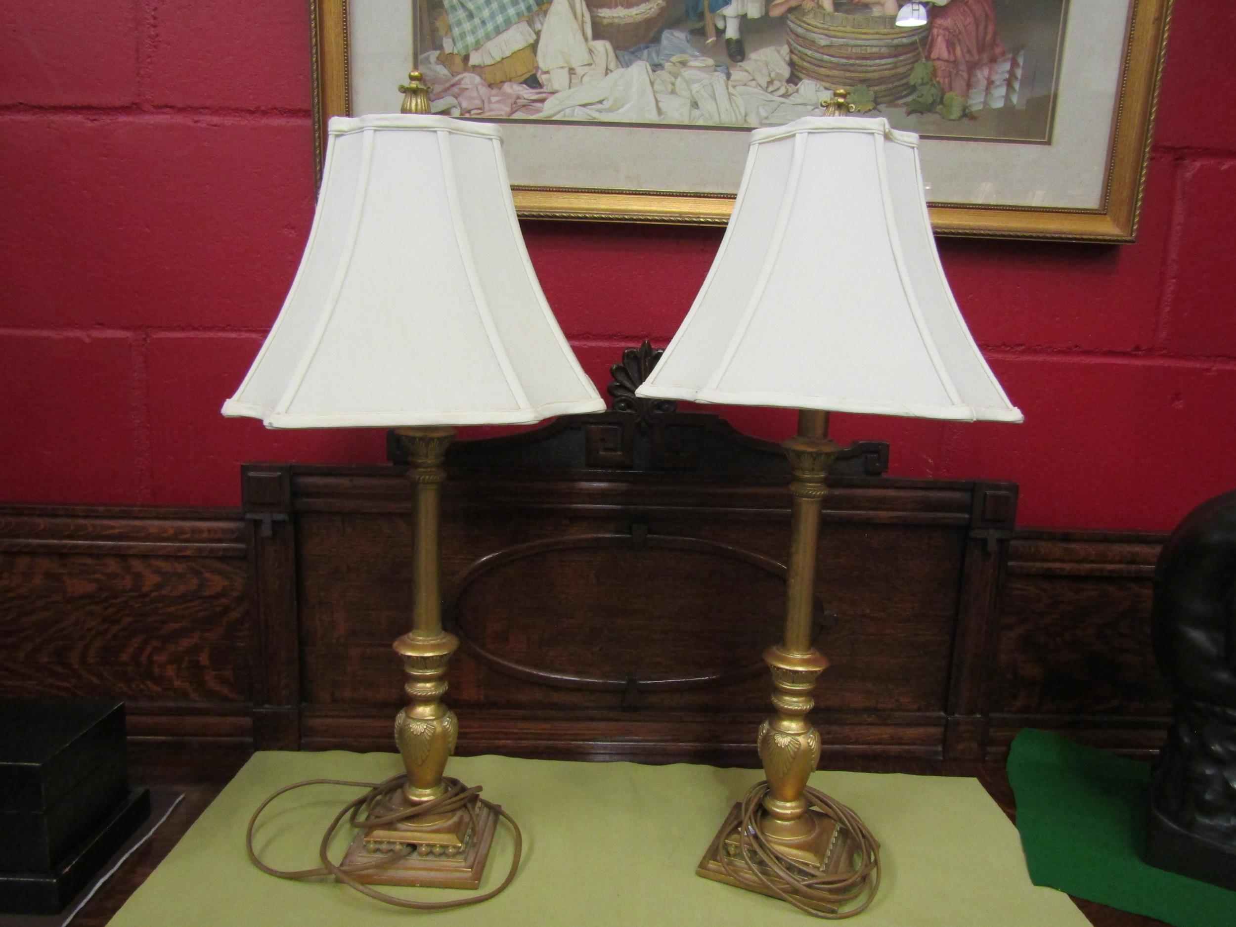 A pair of decorative gilt table lamps with cream shades