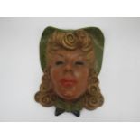 An Art Deco wall mask of female with blonde curly hair in a green hat, wearing red lipstick and a