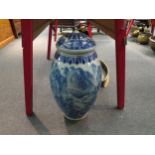 A large floor standing Chinese blue and white jar with lid decorated with river and mountain scenes.