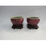 A pair of Oriental red glazed bowls on hardwood stands, 13cm diameter