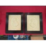 A pair of white plaster relief moulded plaques in black reeded frames