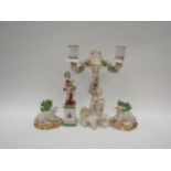 A pair of porcelain lambs with gold anchor mark to base, a putti holding grapes and standing atop