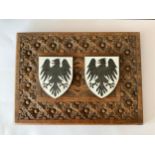 A carved oak plaque with two applied enamel on brass eagle shields, thought to be German, 22cm x