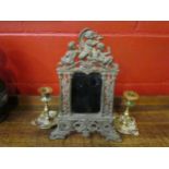 An elaorate heavy metal mirror adorned with cherubs and a pair of ornate brass candlesticks