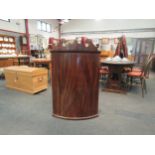 A Georgian mahogany bow fronted wall-hanging corner cabinet, scrolled crest over single door opening
