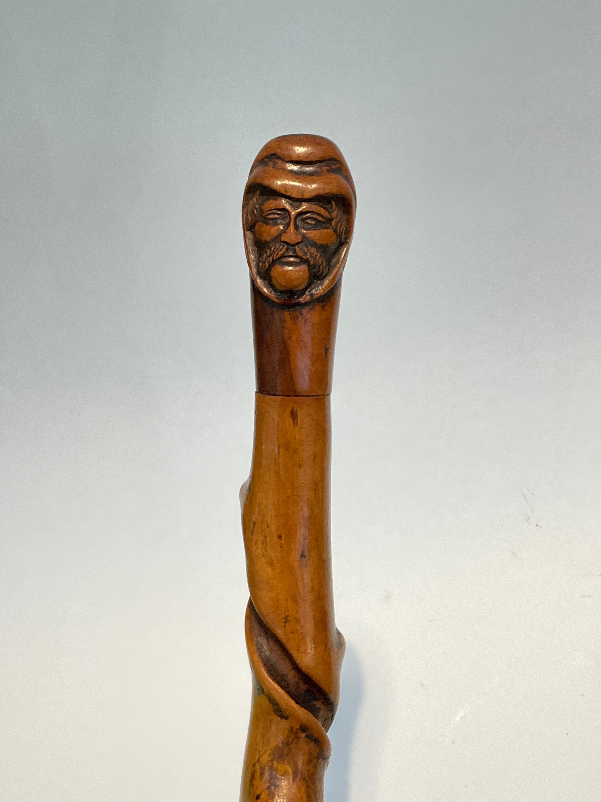 A knarled twisted wood walking cane with carved double ended mask of a man, 92cm long