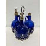 A George V silver plated trefoil-shaped three bottle decanter stand, with three Bristol blue