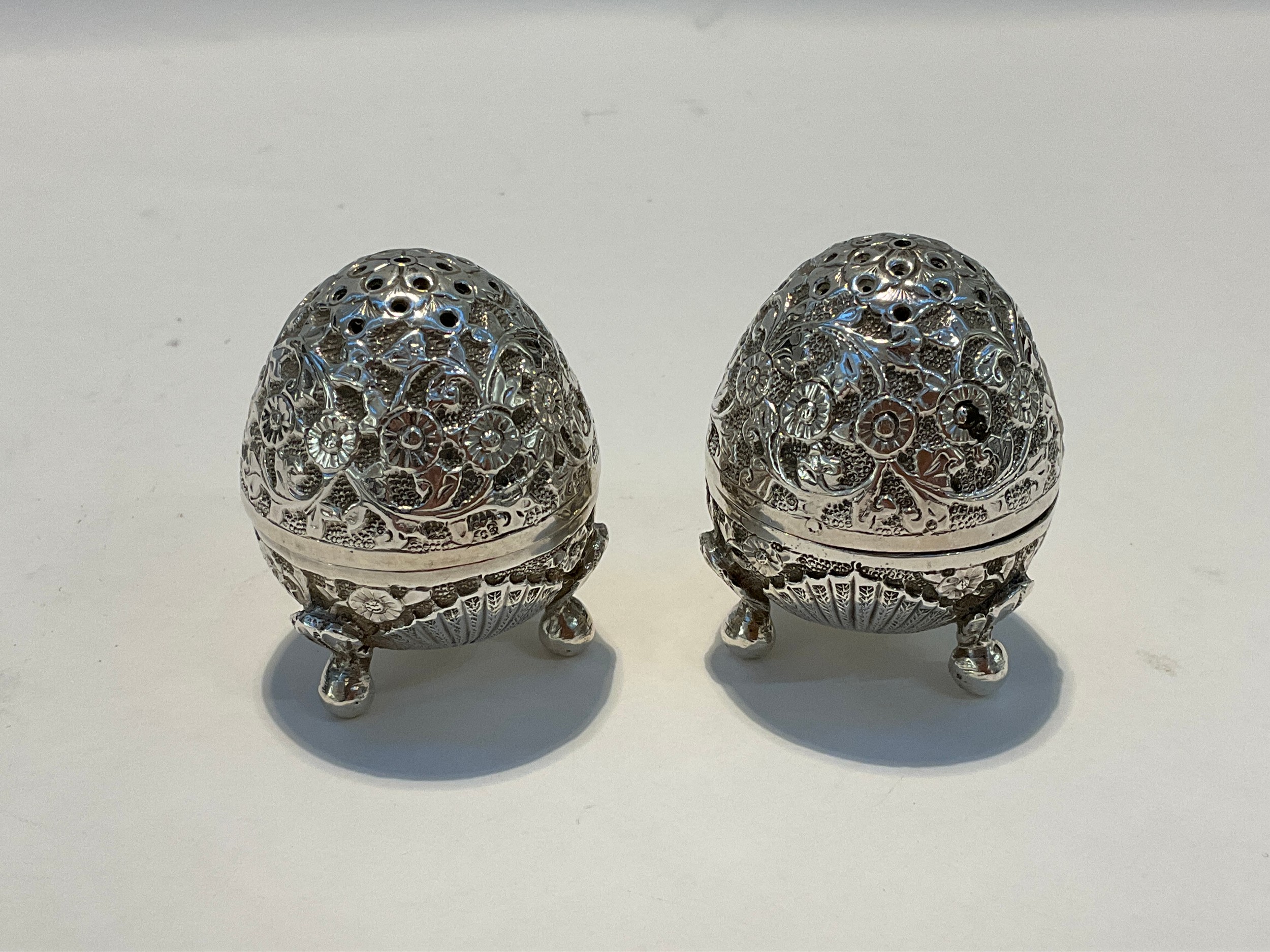 A pair of white metal egg form salt and pepperette shakers, all over foliate and floral design,