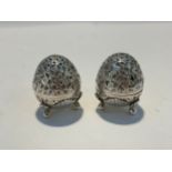 A pair of white metal egg form salt and pepperette shakers, all over foliate and floral design,