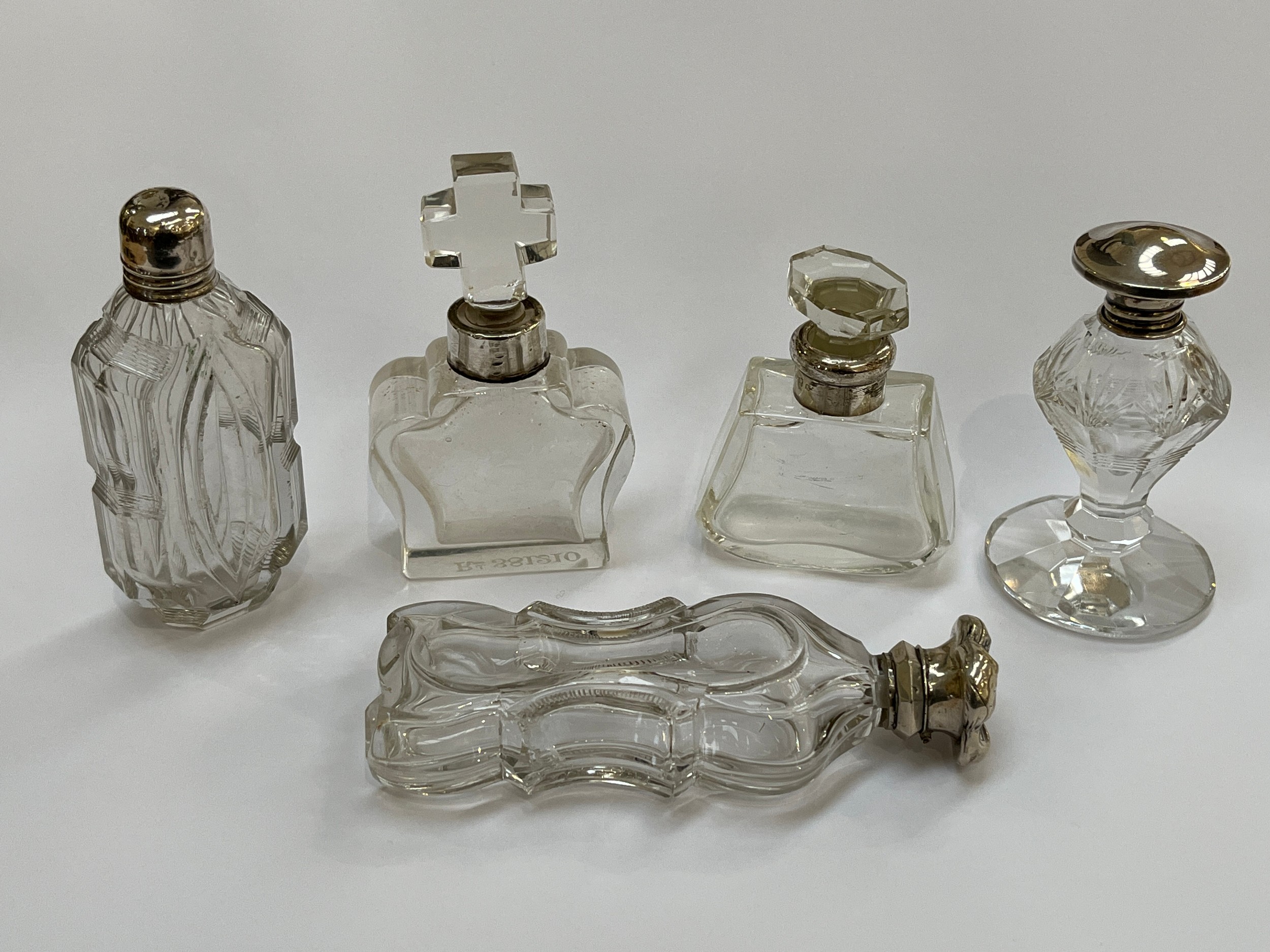 Five clear glass scent bottles, one with cross-form stopper, white metal and silver fittings