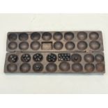 A carved wood Oware game set, played with small pebbles dipped in sand and earth, East African