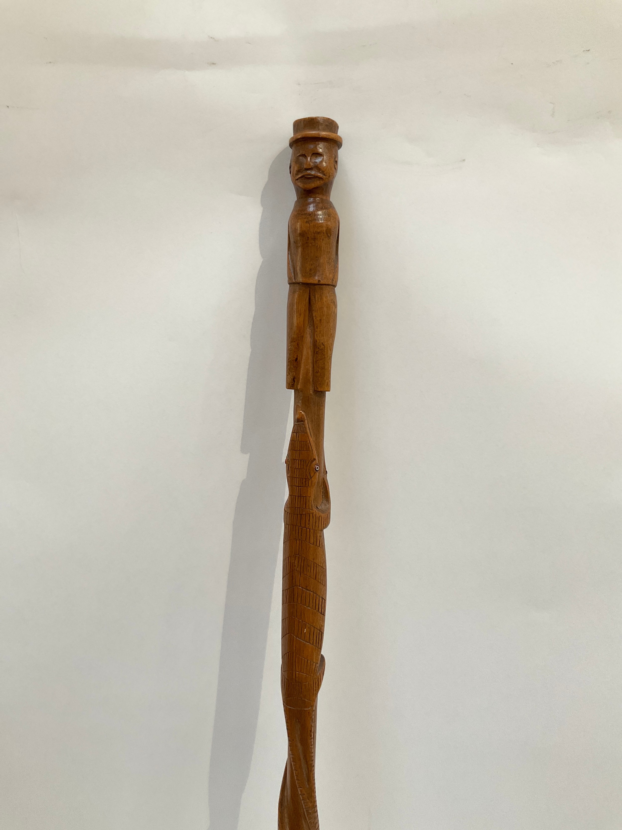 A European carved wood walking cane the carved handle as a man in a hat with a crocodile and snake
