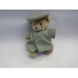 A small jointed teddy bear in pale blue coat and hat