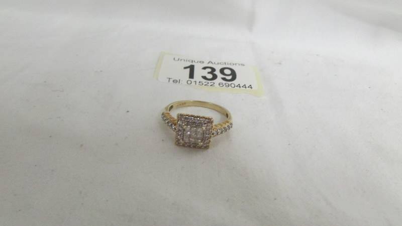 A diamond ring in a square design with princess cut stones and round cut stones in 9ct gold. size R.