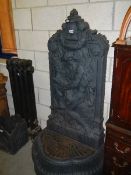 A Decorative cast iron fountain in 2 pieces. The back depicting a man with a fish on an oval base.
