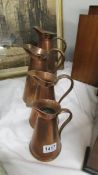 A set of four graduated copper jugs.