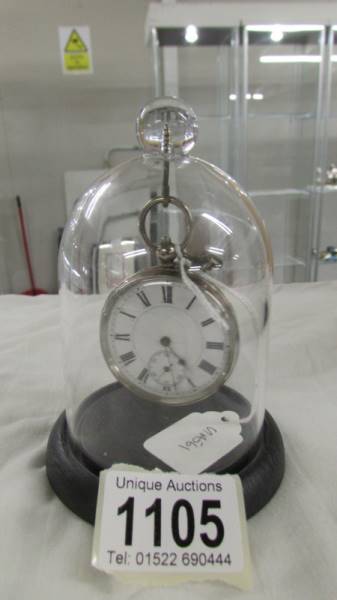 A silver pocket watch in plastic dome stand.