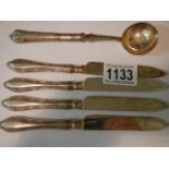 A silver sugar spoon and four silver handled knives.