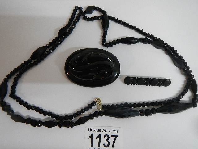 Two black Whitby jet style brooches and a black necklace.