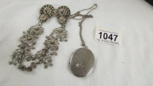 A silver cloak pin and a silver locket on chain.
