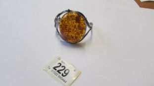 A silver bangle with large amber coloured stone.