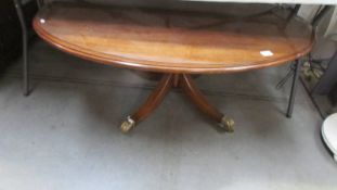 An oval glass topped coffee table with brass lion paw feet, COLLECT ONLY.