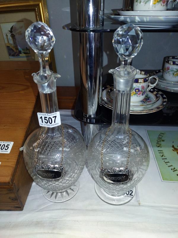 A pair of cut glass decanters, one stopper has chips to the bottom. With Sherry and Port labels.