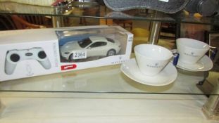 A Maserati remote control car together with two Maserati tea cups and saucers.