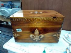 A dovetailed pine box with fleur de lys engraving and crude painted wording around the lid reading