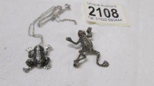 A silver frog pendant on a silver chain and a silver frog brooch.