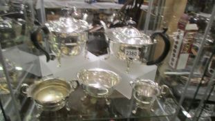 A three piece silver plate tea set, another teapot and a sugar bowl.