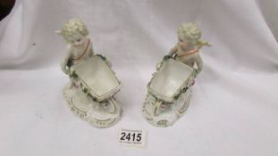 A pair of continental porcelain cherubs pushing wheel barrows.