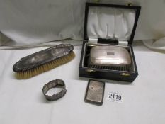 A cased silver backed brush, another silver backed brush, a silver card case and a silver napkin