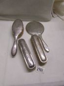 A silver backed vanity set comprising hand mirror and three brushes,