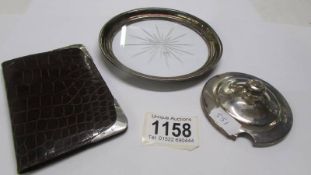 A glass coaster with silver rim, a card case with silver corners and a silver jam pot lid.