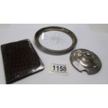 A glass coaster with silver rim, a card case with silver corners and a silver jam pot lid.
