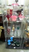 Three shelves of assorted coloured glass ware including baskets, vases etc.,
