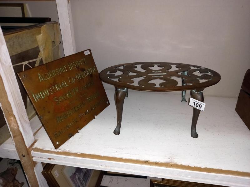 A Brass Aldershot co-op sign and a large oval brass trivet.