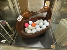 A carved wooden bowl with swan head handle and a quantity of golf balls.