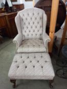 A deep buttoned wing armchair with footstool.
