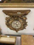 An ornate gilded wall bracket with plaque of children in centre.