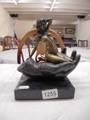 A bronze nude figure sitting on a hand on a marble base.