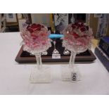 A pair of glass candleholders with cranberry glass shades.