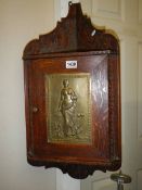 A small oak hanging corner cupboard with art nouveau style metal panel in door.