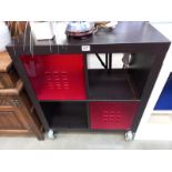 A black ask finished storage unit with dark red plastic drawers.